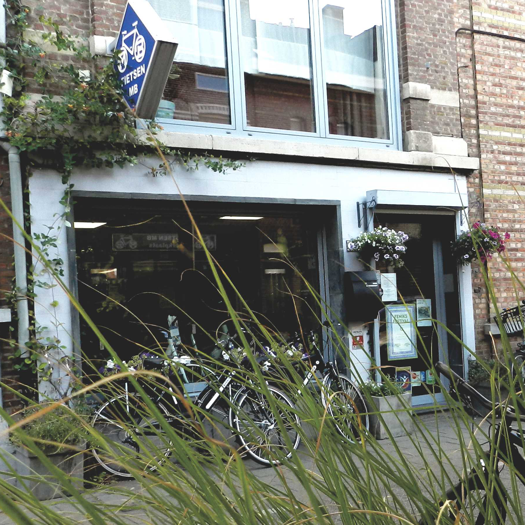 U ziet de fietsenwinkel Fietsen MB in Mortsel op deze foto. U ziet de vitrine, de inkomdeur en het logo